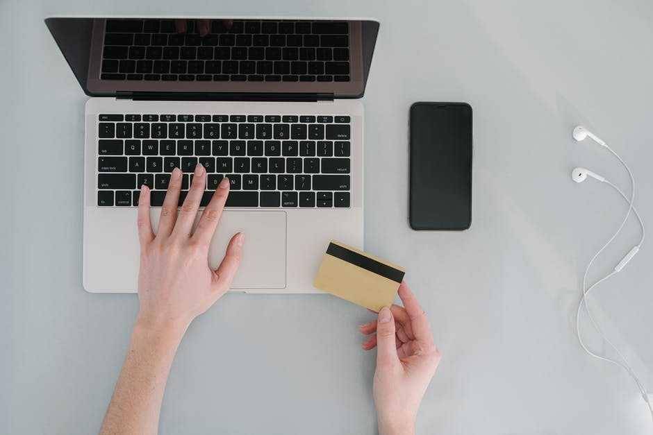 ilustrasi laptop dan kartu debit yang sedang dipegang orang (pexels.com/Mikhail Nilov)